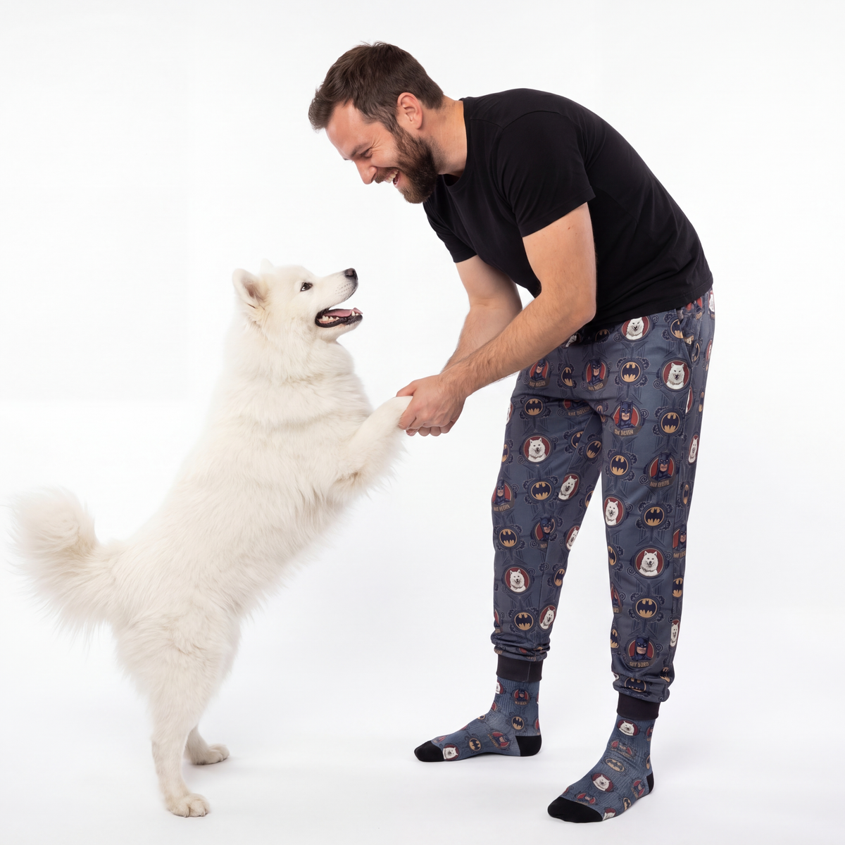 Man in Dark Knight sweatpants interacting with a white dog on a white background