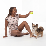 Woman in pajama set sitting on the floor with a small dog, holding a yellow ball