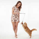 Woman in a cat-themed pajamas playing with a cat toy against a white background