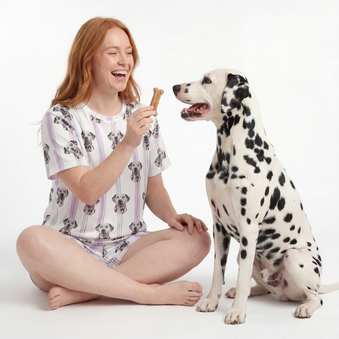 Woman in pajamas sitting on the floor with a Dalmatian dog, holding a treat.