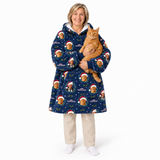 A woman wearing a navy blue hooded robe with a festive gingerbread man and Santa Claus print, holding an orange tabby cat. She is standing against a solid white studio background.