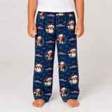 A child wearing navy blue Christmas-themed lounge pants with a repeating print of Santa, a dog, and the text 'Merry Christmas Again', shown against a plain light gray studio background.