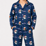 A person wearing a navy blue long-sleeve pajama set with a Christmas-themed dog print, featuring the text 'CHRISTMAS VACCINE' and illustrated dogs in Santa hats and wreaths, against a plain light gray background.