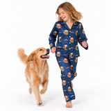A young girl wearing a navy blue pajama set with a Christmas dog print is walking barefoot next to a golden retriever dog on a white studio background.