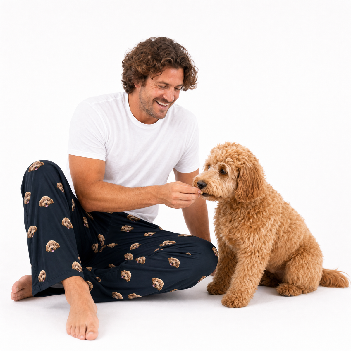 Black adult pants theme – person in dog-print pajamas offering treat to curly-haired dog.