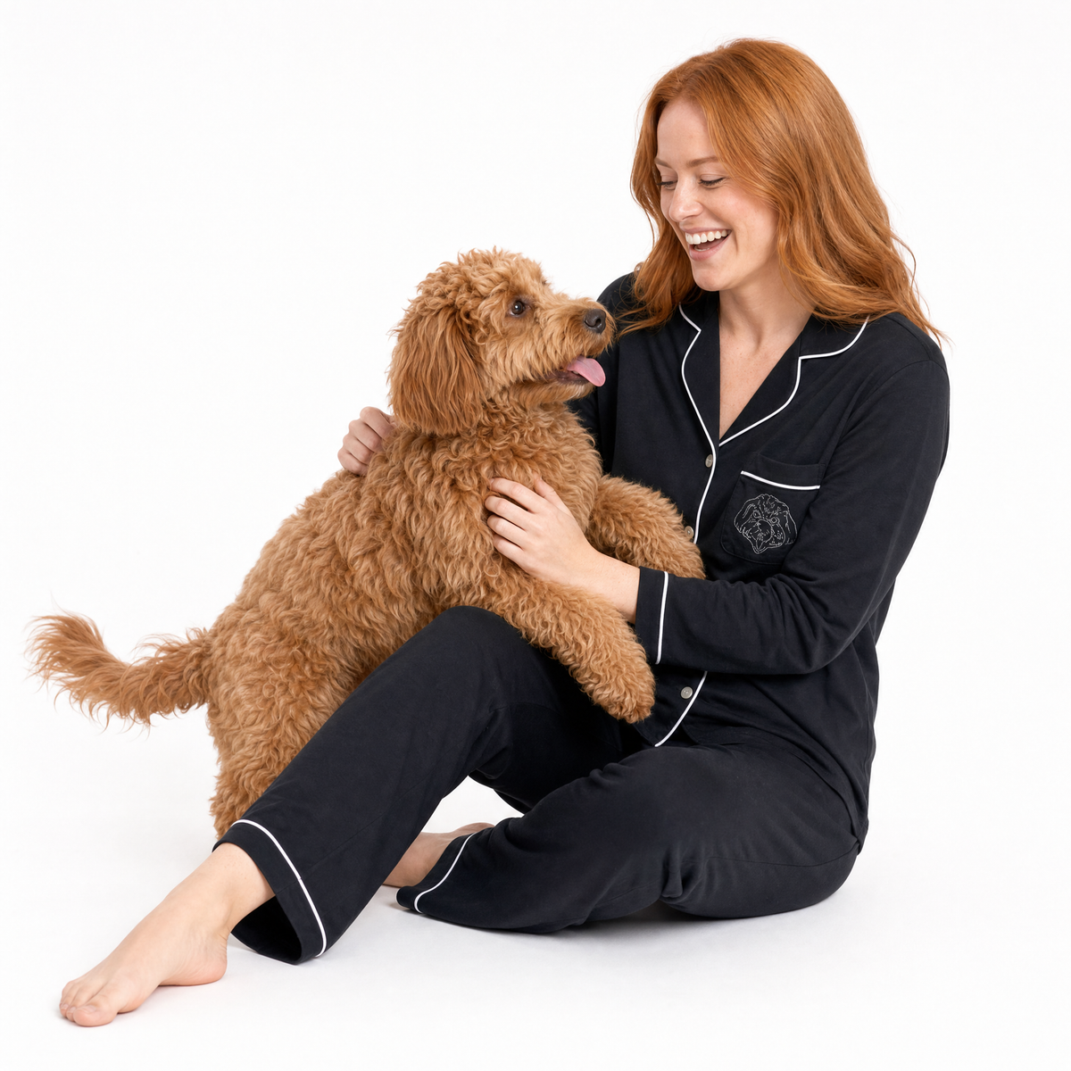 Woman in black pajamas sitting with a brown dog on a white background