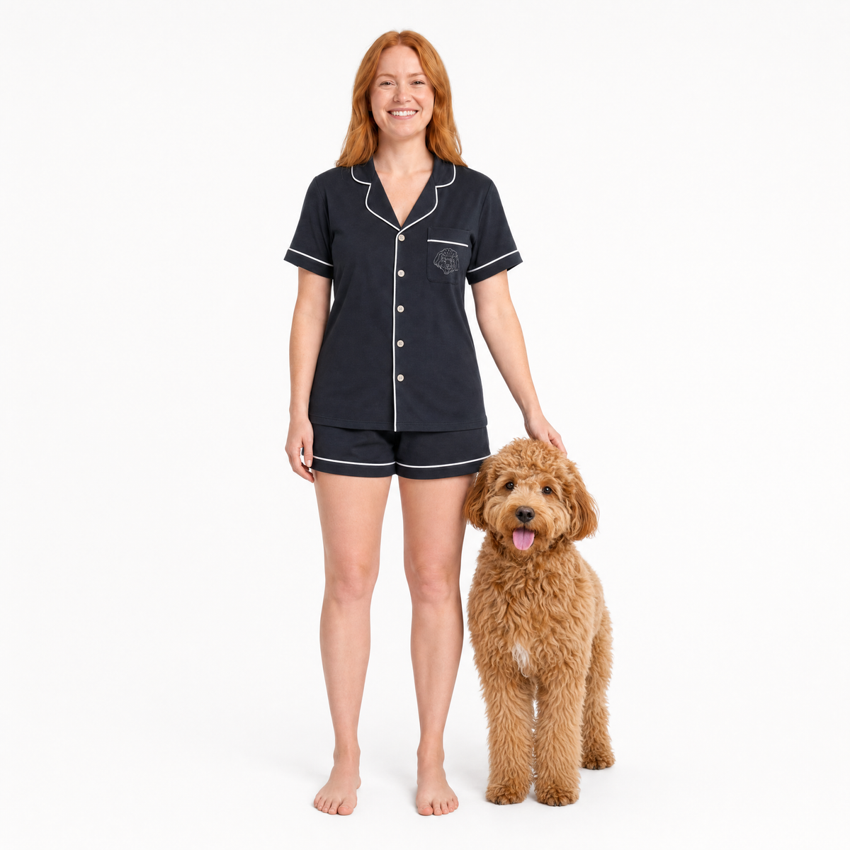 Woman wearing black pajamas with white piping standing next to a brown dog on a white background