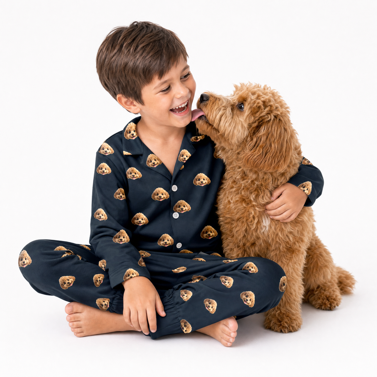 Child in black pajamas with dog face pattern sitting on a white background with a brown dog.