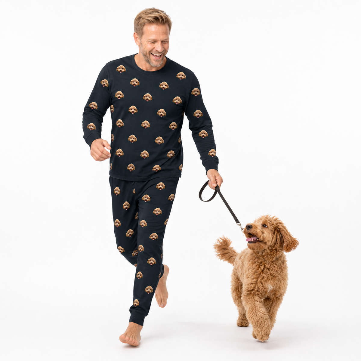 Man wearing black jogger pajamas with brown bear patterns, walking a brown dog on a white background