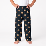A person wearing black pajama pants with an all-over repeating print of small tan and brown dog faces, standing barefoot against a clean white studio background.