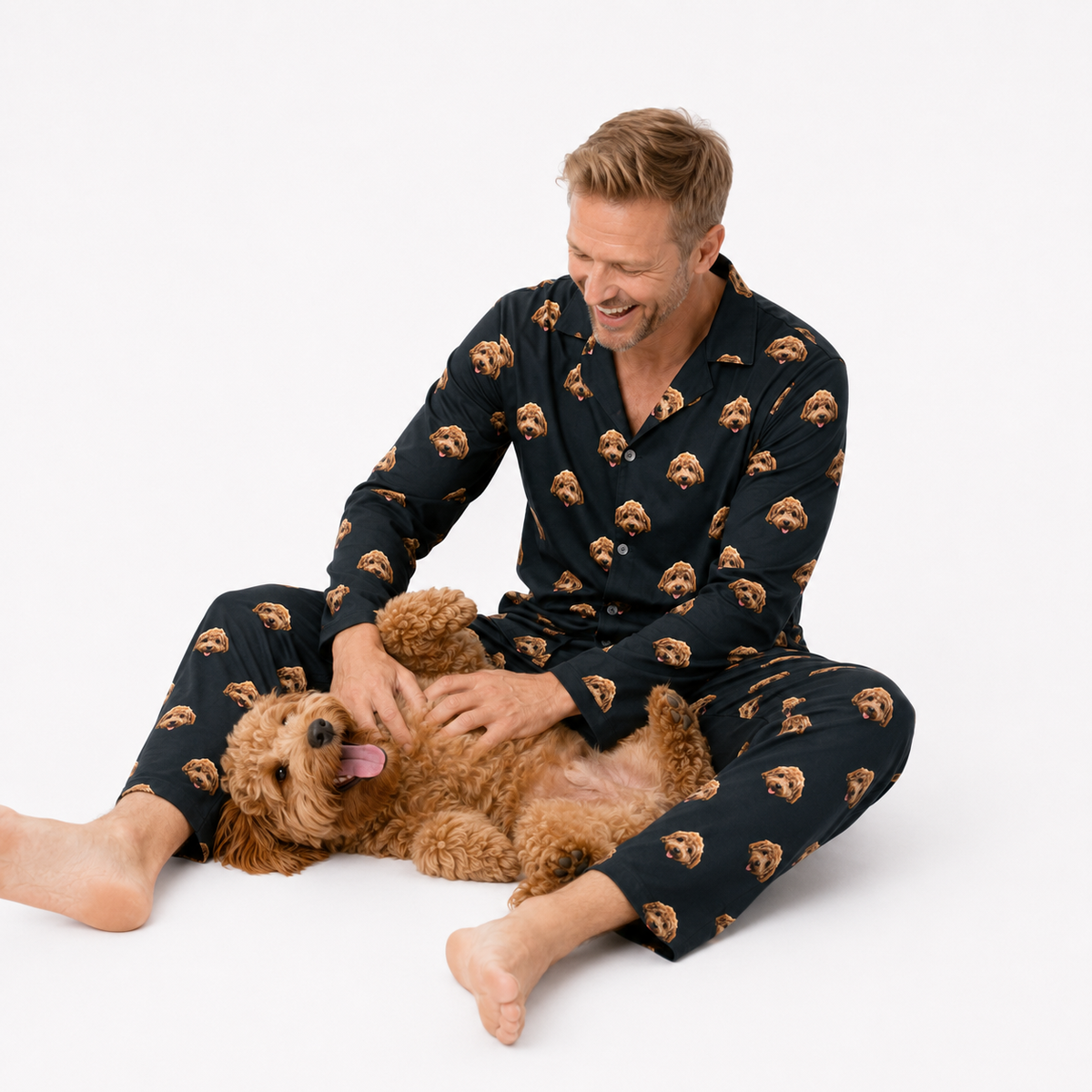 Man wearing a black pajama set with bear patterns, sitting on a white background with a dog.
