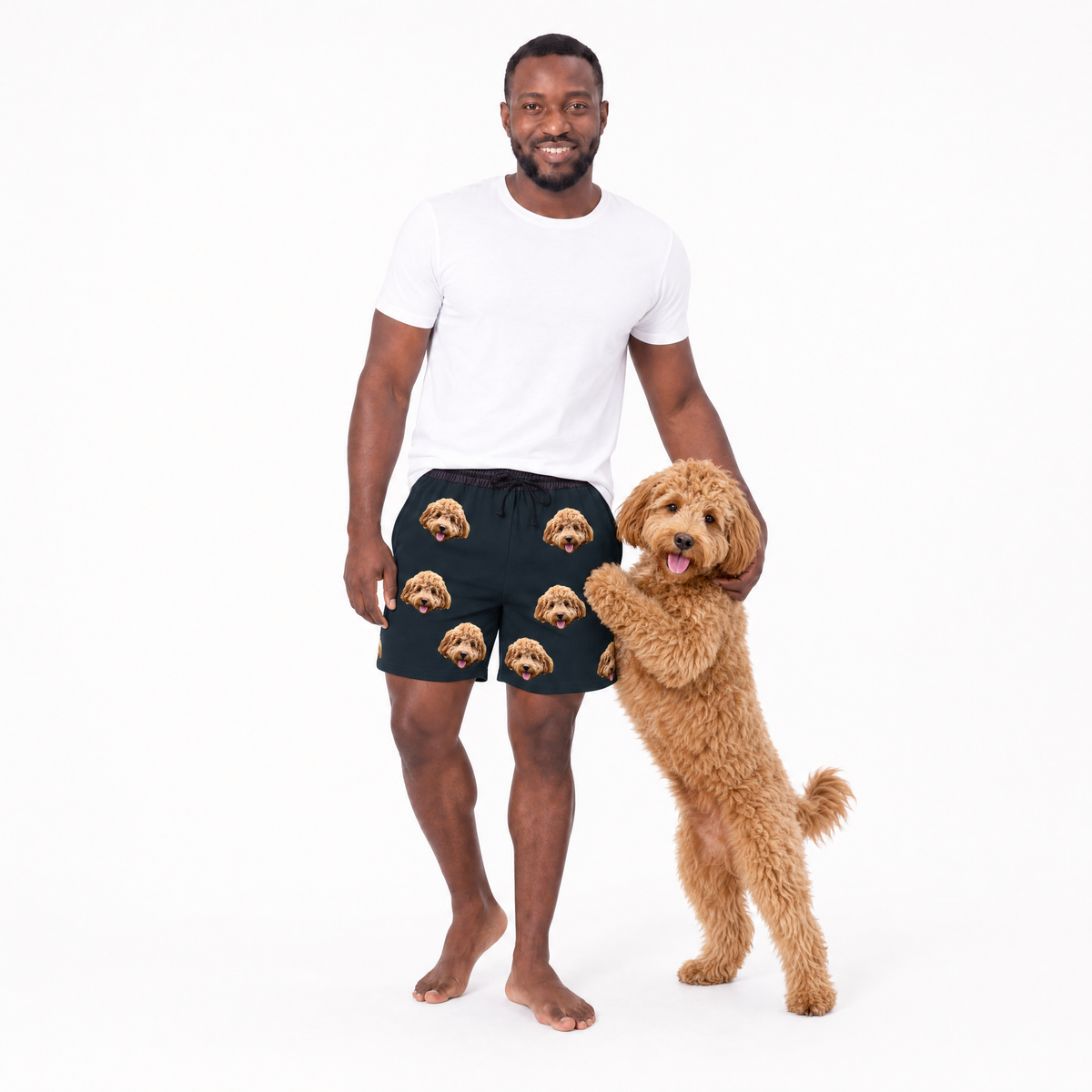Man wearing black shorts with dog pattern standing next to a dog on a white background