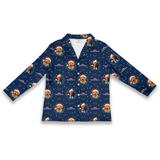 A long-sleeve button-front shirt in navy blue with an all-over Christmas dog print, featuring golden retriever illustrations wearing Santa hats and surrounded by snowflakes, green holly leaves, and purple snow globes.