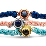 Close up of braided bracelets with a black bead charm in 3 colors.