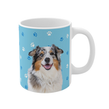 Light blue ceramic mug with paws pattern, featuring a smiling, multicolored Australian Shepherd [LightBluePawsImageCutOut]