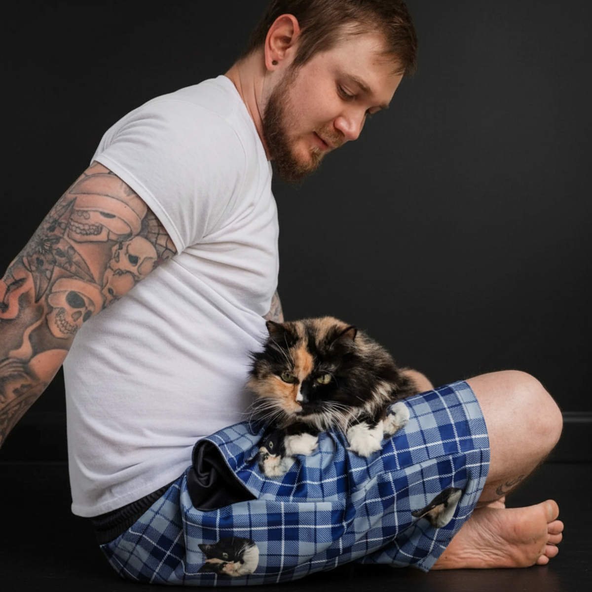 Man sitting with a cat on his lap, he is wearing sweatshorts.