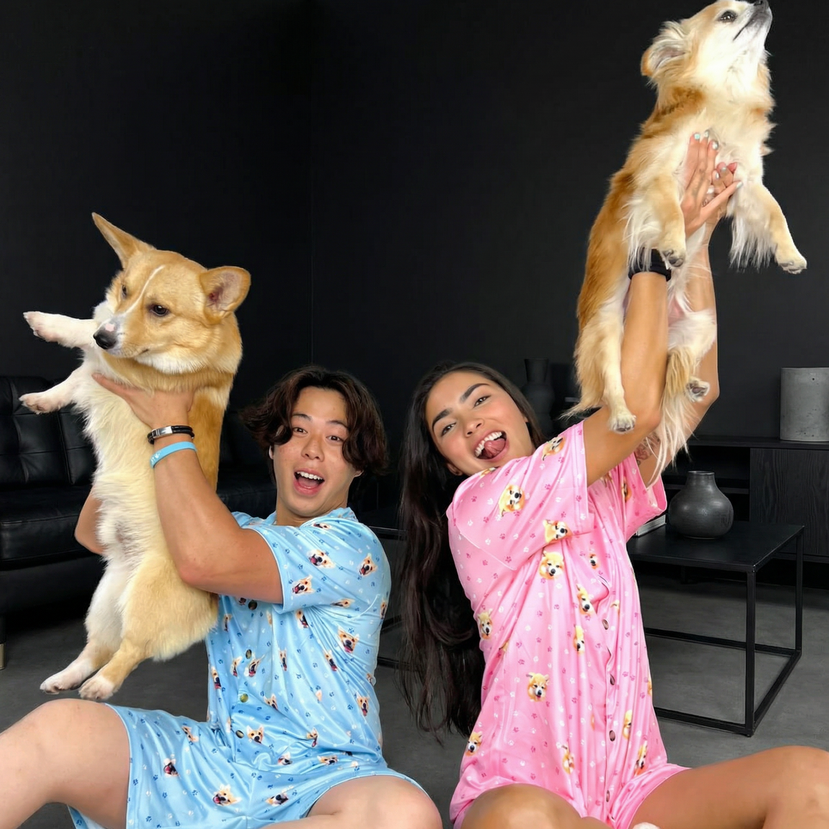 Two people wearing pajamas with two dogs, one in each arm.