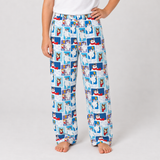 A person wearing loose white pants covered in a repeating blue-and-white collage print of cartoon dogs, standing barefoot against a light gray studio background.