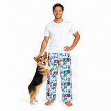 A man wearing a white t-shirt and light blue pajama pants with a cartoon dog print stands next to a corgi on a white studio background.