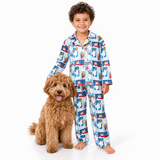 A young boy wearing a long-sleeve pajama set with a blue, red, and white cartoon dog pattern, standing next to a fluffy brown dog on a solid white background.