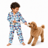 A young boy wearing a light blue pajama set with a cartoon dog print is playfully pulling a tan poodle on a rope against a solid white background.