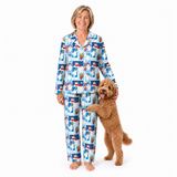 A woman wearing a matching long-sleeve pajama set with a dog printed pattern, standing barefoot on a white studio background next to a small brown dog.