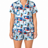 A woman modeling a matching short-sleeve button-front pajama top and shorts set with a blue-toned winter cartoon print featuring polar bear illustrations.
