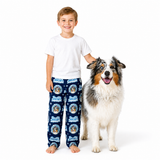 A young boy and a large Australian Shepherd dog stand barefoot against a white studio background. The boy is wearing a white T-shirt and navy blue pajama pants with a repeating circular dog print and the words 'Best Friends'.