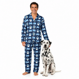 A man wearing a navy blue long-sleeve pajama set with a repeating cartoon dog pattern stands barefoot next to a Dalmatian dog on a plain white background.