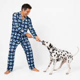 A man wearing blue patterned pajamas plays tug-of-war with a Dalmatian dog on a white studio background.