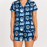 A model wearing a two-piece short-sleeve pajama set with a blue background and a repeating 'Frosted Snowman' dog print, shown against a plain light gray studio background.