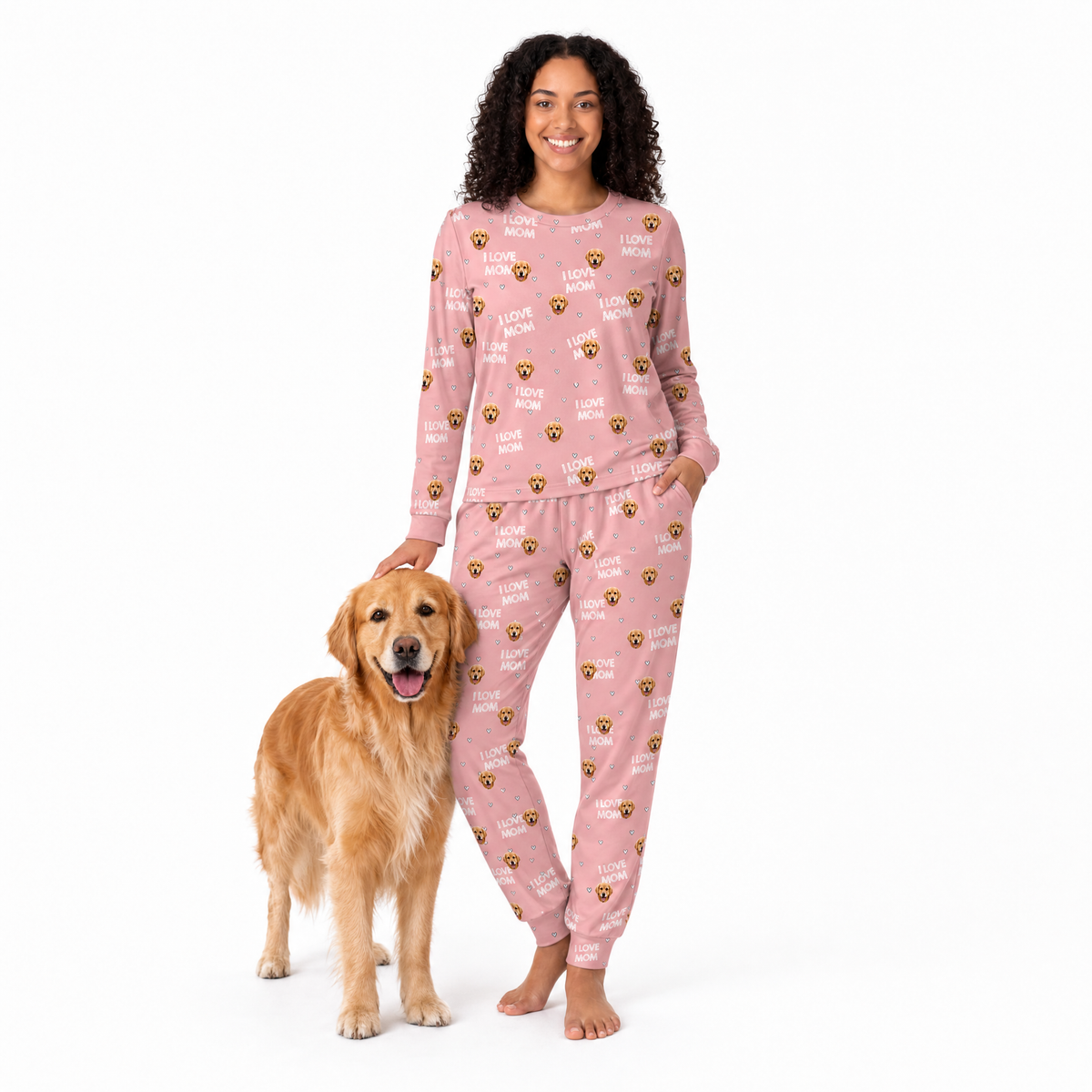 Woman wearing pink jogger pajamas with dog patterns standing next to a golden retriever on a white background