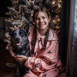 Child wearing a Light Pink Paws hooded blanket hugging a black and gray dog in front of a lit Christmas tree.