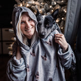 Woman wearing a Slate Gray hooded blanket cuddling with a black and gray dog in front of a lit Christmas tree.