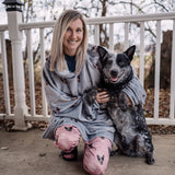 Woman wearing a Slate Gray hooded blanket kneeling on a porch beside a black and gray dog