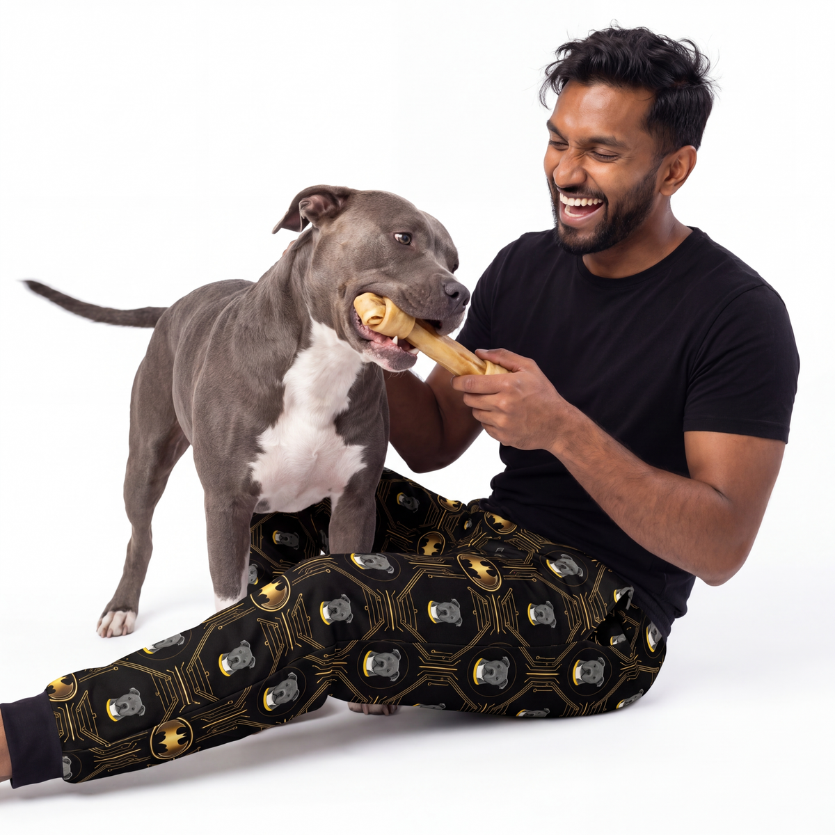 Man and dog playing with a bone wearing  Iconic Batman sweatpants on a white background 
