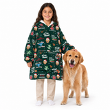 A young girl wearing a dark green Christmas-themed hooded blanket sleeper stands next to a golden retriever dog on a white studio background. The sleeper features a festive print with Santa Claus, reindeer, snow globes, and holiday quotes like 'Dad, Santa Claws!'.