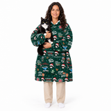 A woman wearing a green Christmas-themed hooded robe with a black and white cat on her shoulder, standing against a plain white background.