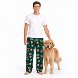 A man wearing dark green Christmas-themed pajama pants with a cartoon dog print stands next to a golden retriever dog on a white studio background. The man is also wearing a plain white t-shirt.