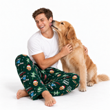 A man and his golden retriever dog sitting on a white studio floor, wearing matching dark green Christmas-themed pajamas with a cartoon dog print.