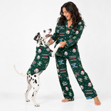 A woman and a Dalmatian dog wearing matching green Christmas-themed pajamas with a print of Santa, dogs, snow globes, and the text 'A Christmas Christmas' on a white studio background.