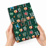 A gift box wrapped in dark green Christmas-themed paper with a pattern of gingerbread cookies in Santa hats, trees, snowflakes, and holiday quotes, tied with twine and held by two hands against a white background.
