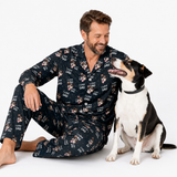 Man wearing a pajama set with dog prints sitting next to a dog on a white background