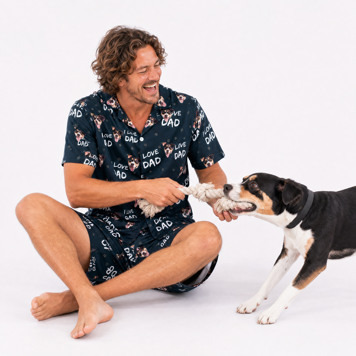 Man wearing a i love dad pajama set with dog patterns, sitting on the floor with a dog.