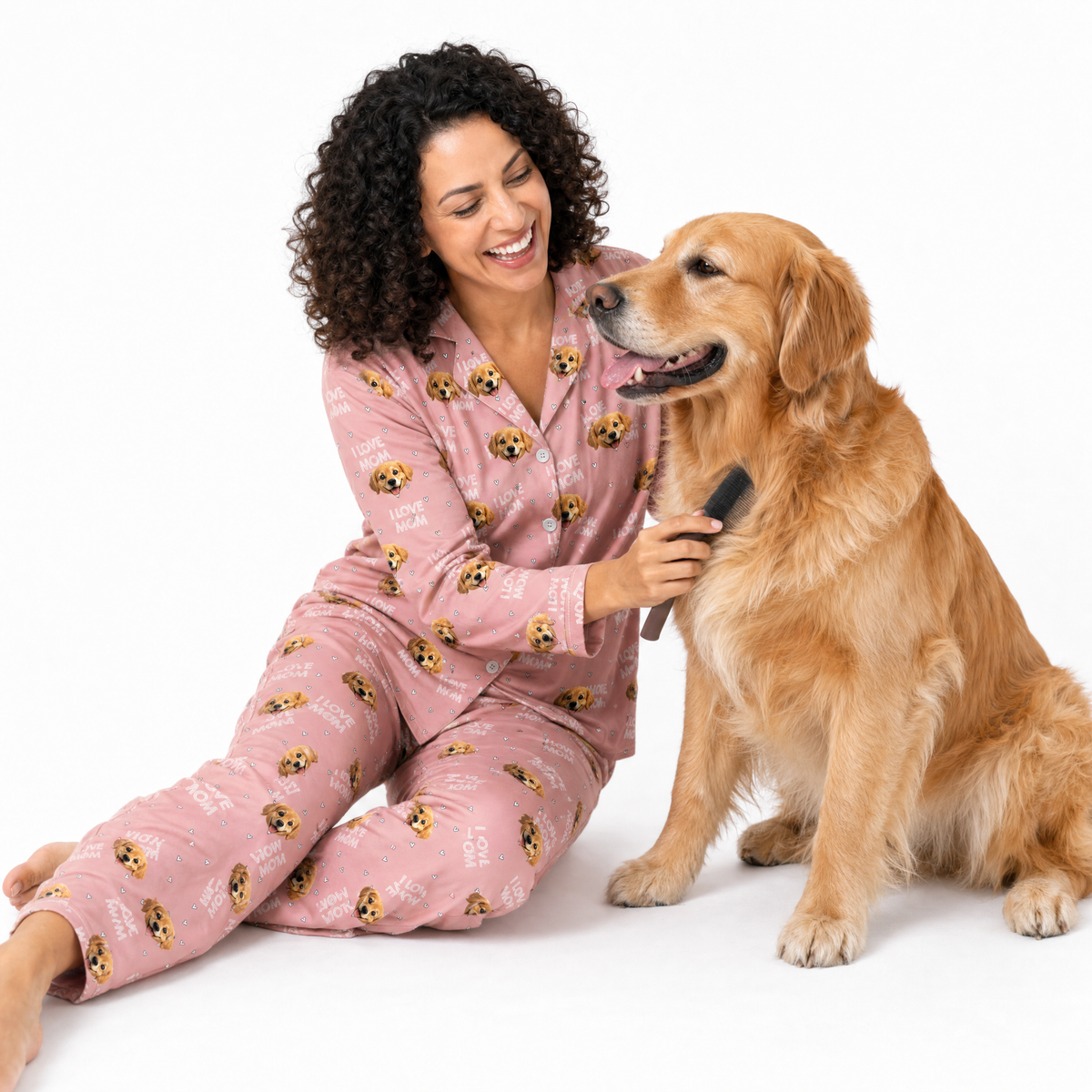Woman in pink pajamas with dog pattern sitting next to a golden retriever on a white background