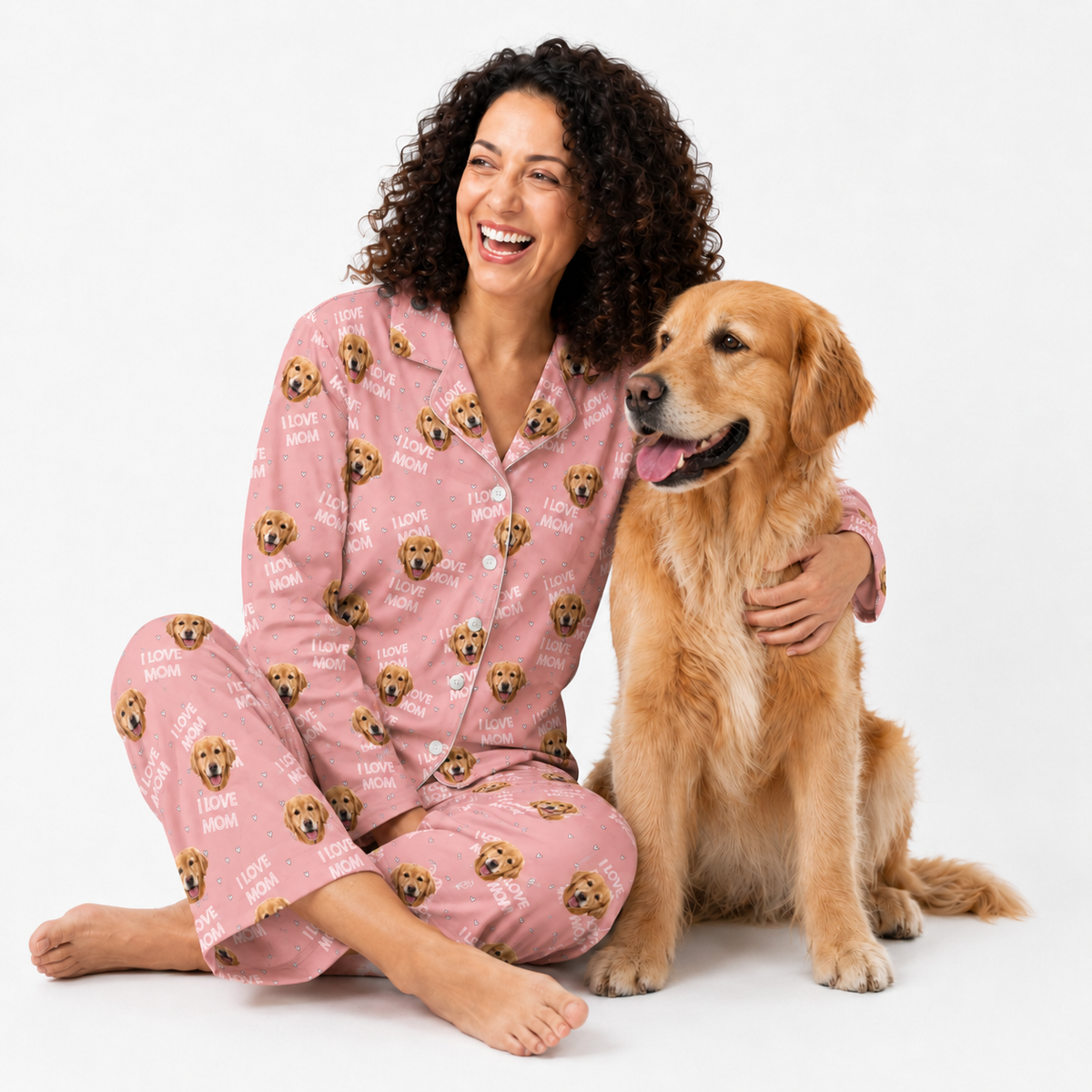 Woman wearing an I Love Mom dog-print pajama set sitting beside a golden retriever.
