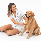 Woman in a white pajama set brushing a golden retriever on a white background