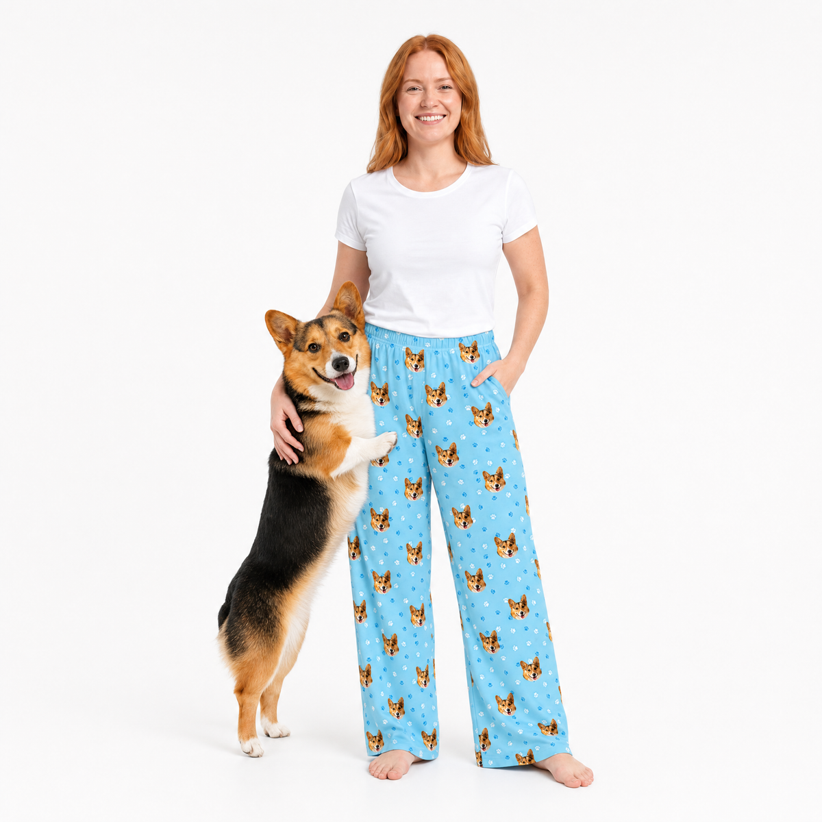 Woman wearing light blue pajama pants with dog pattern, standing next to a dog on a white background