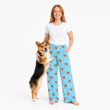 Woman wearing light blue pajama pants with dog pattern, standing next to a dog on a white background