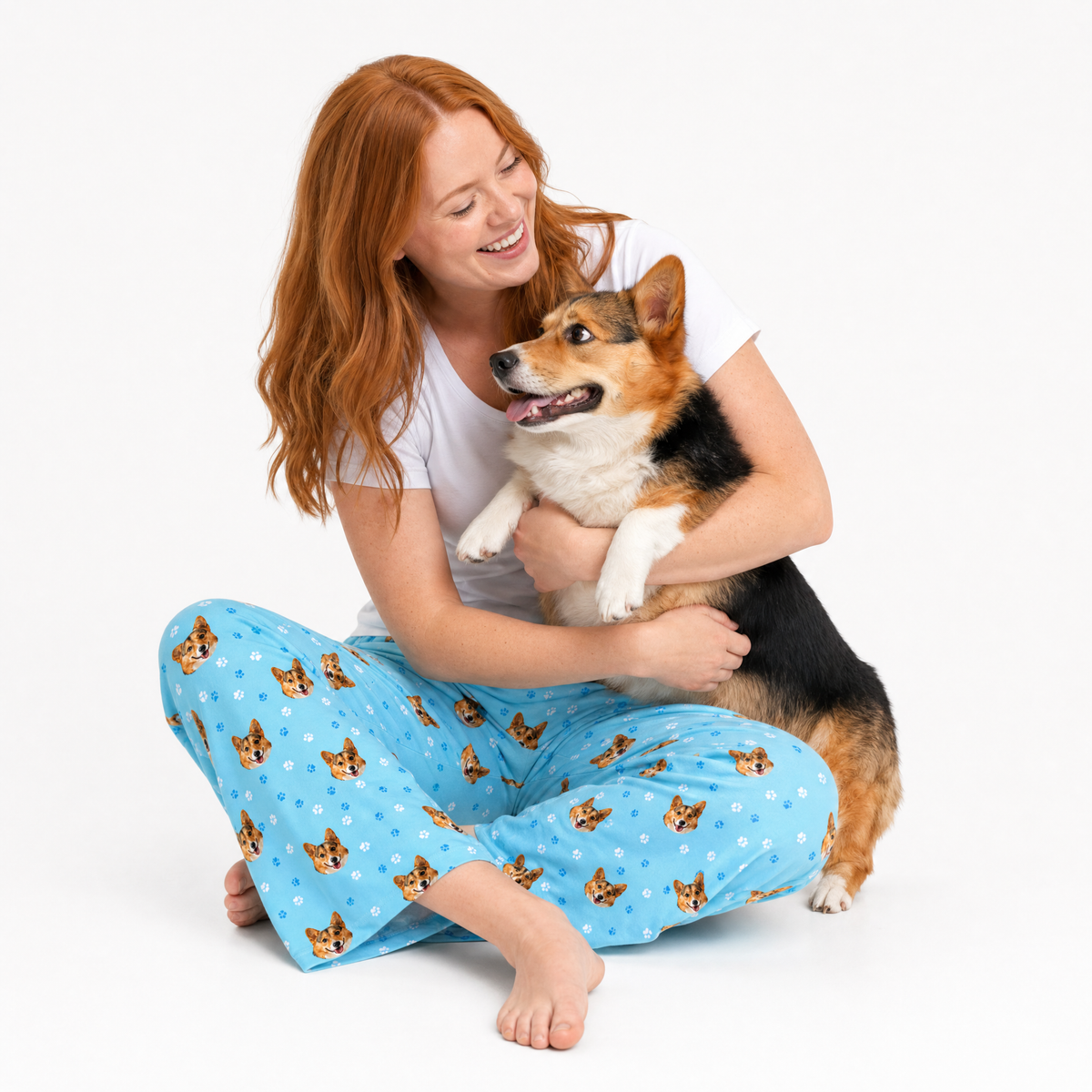 Sky blue corgi theme – person in corgi-print pajamas cuddling tricolor corgi.
